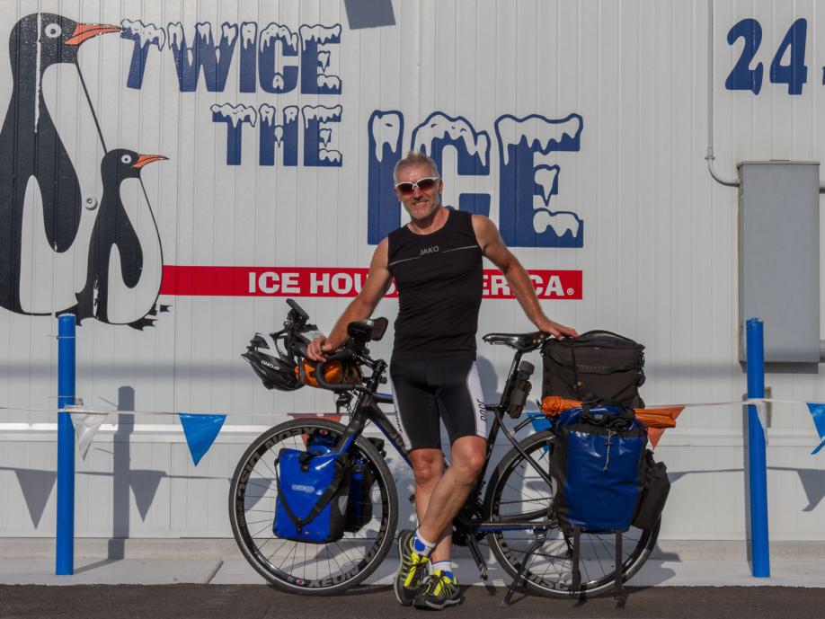 Thomas mit Fahrrad vor einer Wandmalerei, die für ein Eis-Event wirbt und Pinguine zeigt.